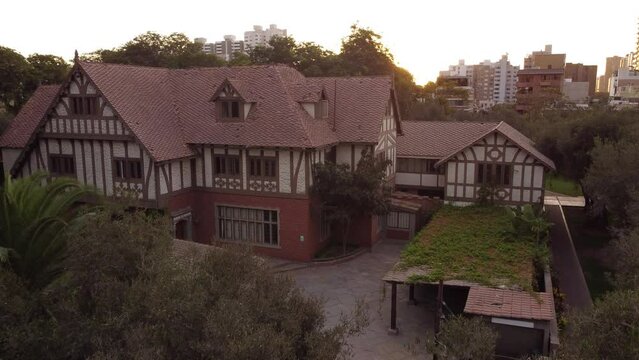 Warm sunset illuminating the facade of a charming tudor style house with urban skyline in the olive grove forest in Lima - Peru