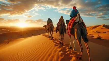 Rolgordijnen A caravan of camels with riders trek across rolling desert dunes under a vibrant sunset sky. © Nuth