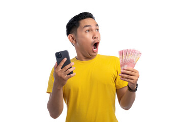 Excited handsome Asian man holding money and mobile phone, looking at copy space with shocked expression isolated on white background