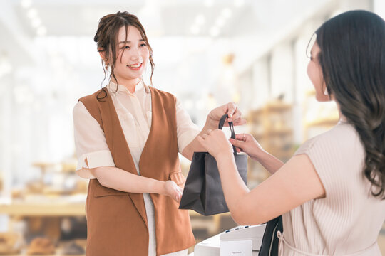 雑貨屋・アパレルショップで買い物・ショッピングをしたお客様に紙袋を渡す販売員・スタッフ
