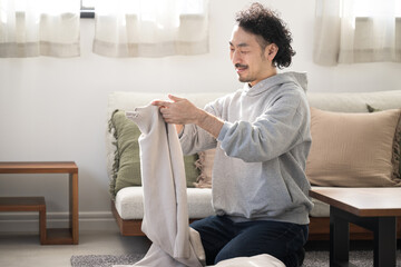 メインビジュアルにも！リビングで洗濯を畳む笑顔で家事をするアジア人(日本人）男性の全身 © kapinon