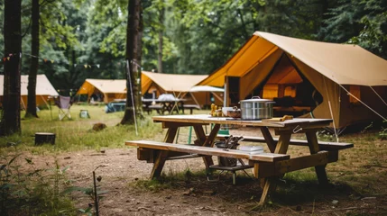 Fototapeten Wooden table against the background of standing tents with outdoor kitchen equipment at a campsite in a natural park. Travel concept. © Alina Tymofieieva