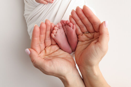 The palms of the father, the mother are holding the foot of the newborn baby in a white blanket. Feet of the newborn on the palms of the parents. Studio macro photo of a child's toes, heels and feet.