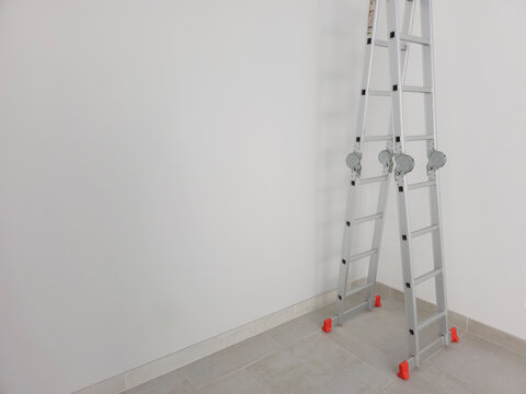 Escalera plegable articulada de aluminio y de fondo una pared blanca/clara. Se puede usar como fondo para un anuncio.