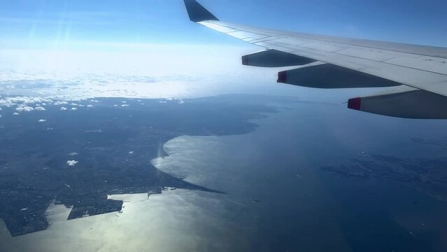 Aerial view from airplane window, wing over coastline with blue sky