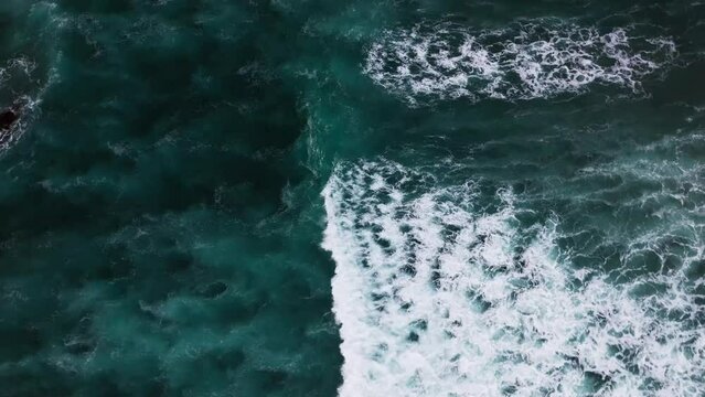 aerial top down video of large and powerful waves crashing down on the rocky shore line on a hot and sunny day by the coast in Hawaii.