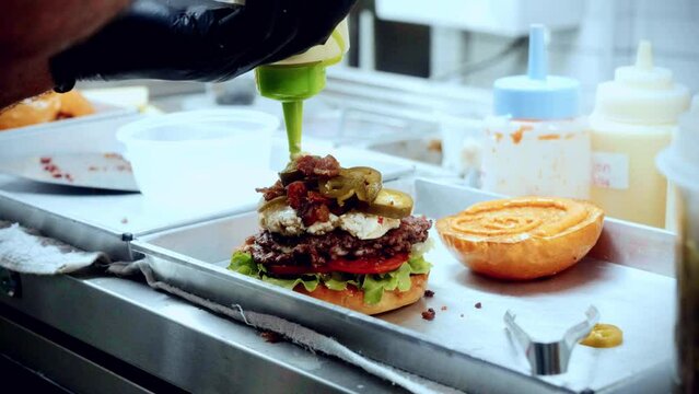4K Cinematic food cooking footage of a chef preparing and making a delicious homemade burger in a restaurant kitchen in slow motion putting the sauce on top of the smashed burger