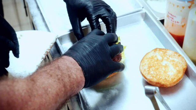 4K Cinematic food cooking footage of a chef preparing and making a delicious homemade burger in a restaurant kitchen in slow motion putting the smashed patty on the bun