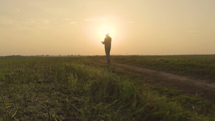 The figure of a farmer in the rays of the setting sun. Sunset in an agricultural field on which a...