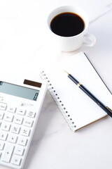 淹れたてのコーヒーを飲みながら、電卓とメモ帳でデスクワークをしているイメージ
