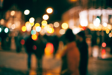 An out-of-focus look at people walking outside in a town at night with with blurs of dotted light all around. - obrazy, fototapety, plakaty