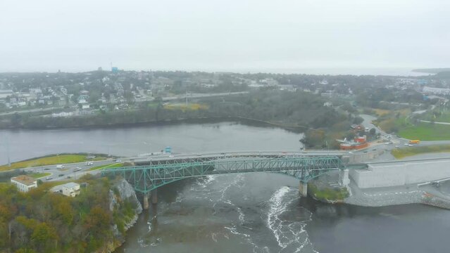 An Aerial shot of the reversing falls bridge with cars passing overtop on a cloudy day.