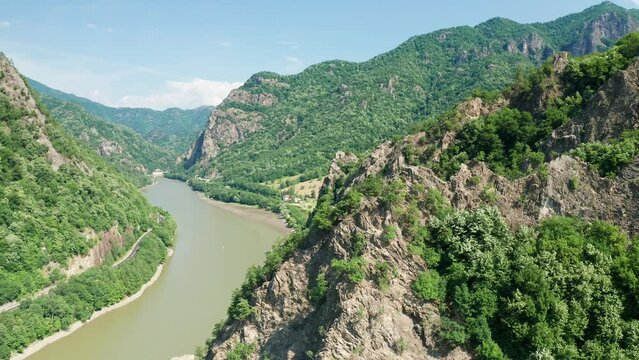 The winding olt river cutting through the verdant valleys and hills, under sunny skies, aerial view
