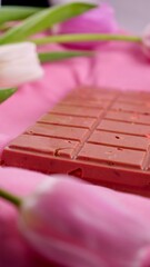 A bar of pink ruby chocolate with sublimated freeze-dried strawberries and almonds and spring tulip flowers . A dessert based on berries and nuts for International Women's Day, March 8, mother's day