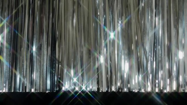 不規則にたなびく銀色のテープで作られた下端が出ているカーテンと踊る光芒,激しい点滅