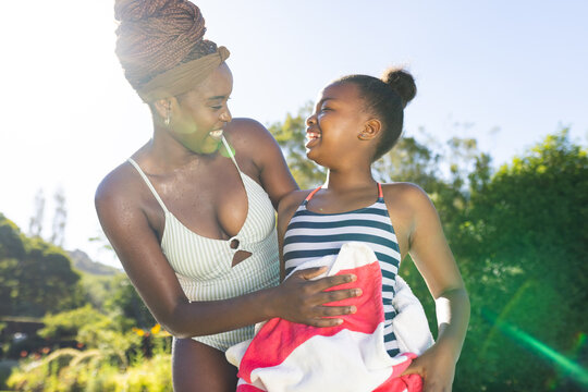 A young African American mother wraps a towel around a daughter after swimming on a sunny day