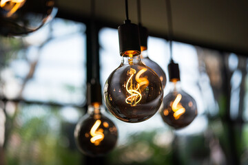 Classic lighting bulbs are glowing in orange warming shade, there are hanging from ceiling for Interior cozy style decoration. Close-up and selective focus.