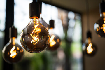 Classic lighting bulbs are glowing in orange warming shade, there are hanging from ceiling for...