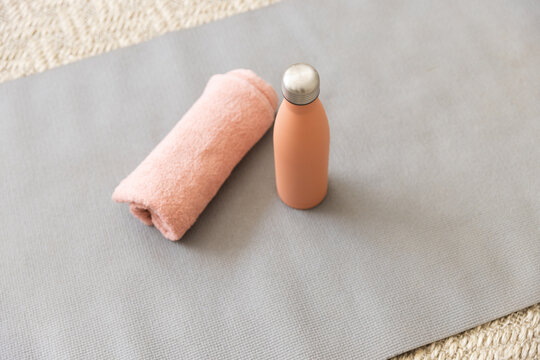 A coral towel and a matching water bottle rest on a yoga mat