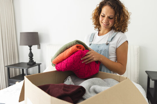 A young Caucasian woman unpacks colorful sweaters from a box and sorts clothes for donation