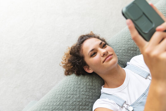 A young Caucasian woman lounges with her smartphone on bed at home, with copy space