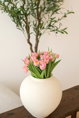 Pink tulips in white vase on wooden table.