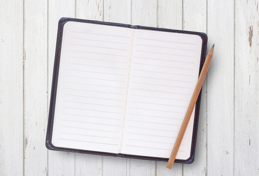 Top view of blank white cover notebook with pencil on white wood table background.