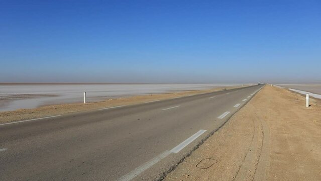 Empty desert road stretching into horizon under clear blue sky, Tunisia