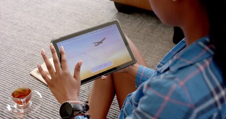 A young African American woman is browsing a travel booking site on her tablet