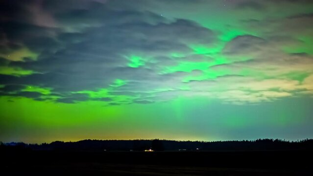 Cumulus clouds drift by under the green glow of the Northern Lights.