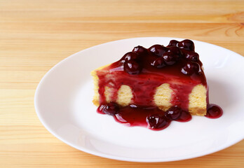 Plate of a slice of delectable baked cheesecake with blueberry sauce on wooden table