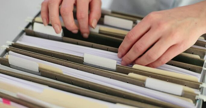 Woman employee sorts through documents in folders from box