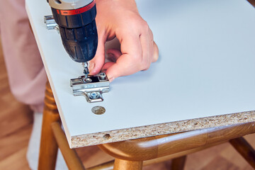 Adjustable hinges are installed in the chipboard cabinet door during flat pack furniture assembly.