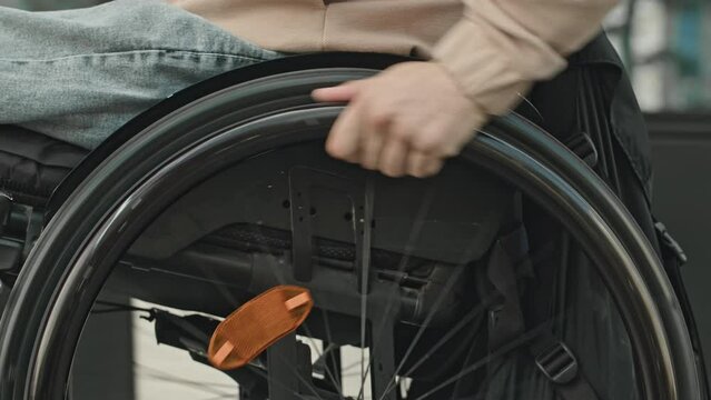 Close up shot of hands of unrecognizable man pushing rims of manual wheelchair while riding outdoors