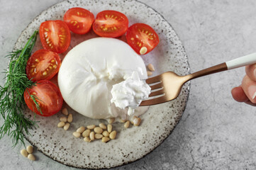 burrata with tomatoes. Caprese salad with tomatoes, burrata cheese and pine nuts. Soft cheese in a burrata bag