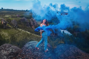 A Woman holds a Blue Smoke bomb in a Hand in the Rocky Landscape. The girl is surrounded by...