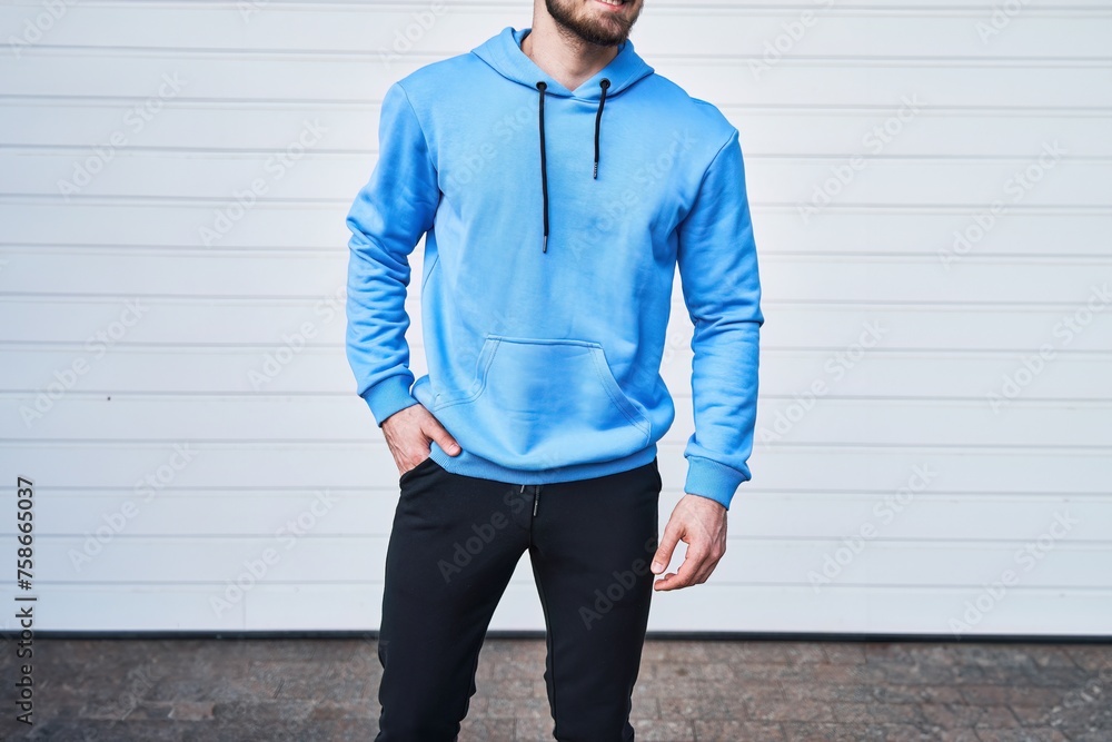 Poster mockup shows a stylish man wearing a blue hoodie and leaning on a white wall. it is perfect for show - Posters
