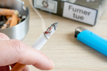 Main de femme tenant une cigarette, paquet de cigarette français, cendrier et briquet.