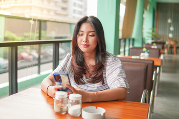 Young Asian woman wearing dress sitting at a restaurant for a breakfast, looking at smartphone in a deep thought with serious face