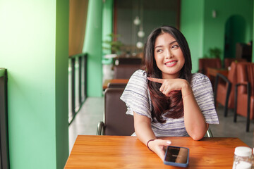 Young pretty Asian woman sitting at a restaurant to have breakfast while using smartphone with finger pointing to her right side