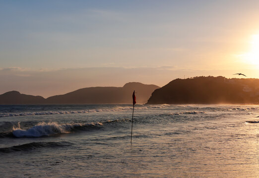 Waves of the Atlantic Ocean at Geriba beach on sunset in Buzios, Rio de Janeiro, Brazil. A red flag on the beach means swimming is dangerous.	