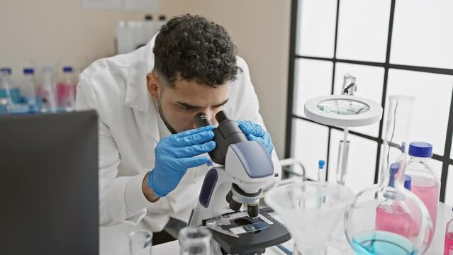 A young hispanic man with a beard works in a laboratory, using a microscope, portraying a professional healthcare setting.