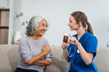 Caucasian female doctor introduces medicine to an elderly Asian patient while seated on a sofa,...
