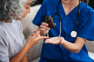 Caucasian female doctor introduces medicine to an elderly Asian patient while seated on a sofa, providing guidance and information about the prescribed medication.