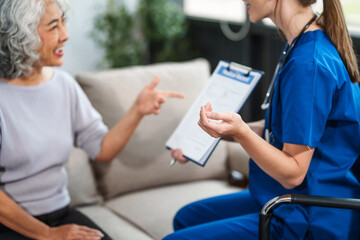 Obraz premium Caucasian female doctor delivers the results of a health check to an elderly Asian patient while they are both seated on the sofa.