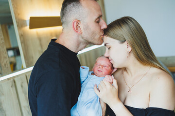 Happy young parents holding their newborn baby in their arms. Romper on a newborn boy. Newborn baby in the hands of mom and dad