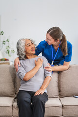 A Caucasian female doctor provides encouragement and advice on maintaining good health to an elderly Asian patient while they sit together on the sofa.