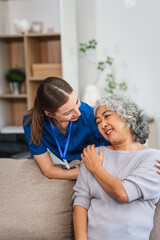 A Caucasian female doctor provides encouragement and advice on maintaining good health to an elderly Asian patient while they sit together on the sofa.