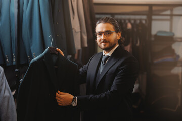 Smiling businessman in glasses chooses to buy suit jacket in classic clothes shop store for men