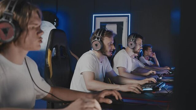 Gamers team playing video game on PC at computer club, cyber sport tournament. E-sport championship. Five guys in headset, left-handed player. Multiplayer online battle, first-person shooter